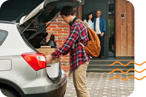 Photo of a teenage boy loading his car trunk while his parents look on from the front porch